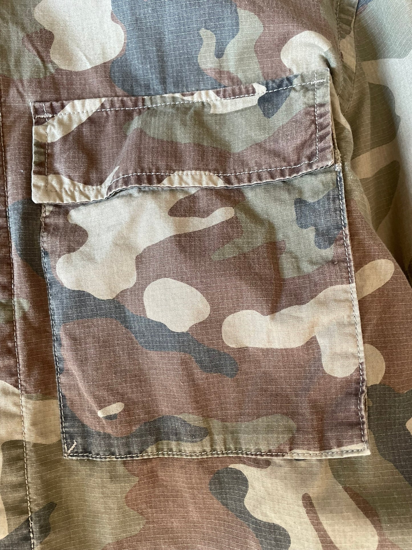 Close-up of a camouflage fabric garment showing a front patch pocket with a flap and stitched seams.